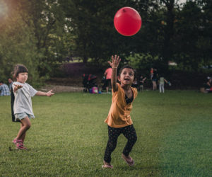 Two children playing in the grass with a red balloon.