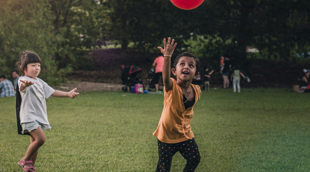 Two children playing in the grass with a red balloon.
